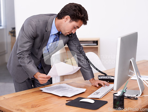 Image of Businessman, phone call and multitasking on computer in office, networking and technology in workplace. Young accountant, talking or landline with paperwork, consultation or finance advice in company