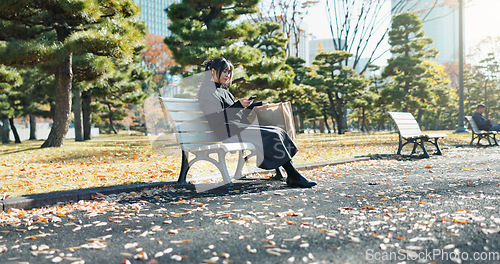 Image of Japanese woman, bench and smartphone in park with relax, happiness and social media in sunshine in city. Female person, sitting and wellness with cellphone in town, streaming and digital technology