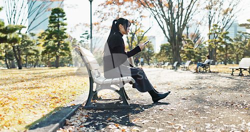 Image of Asian woman, walking and relax on park bench with phone for social media, communication or networking. Female person sitting with mobile smartphone for online search, streaming or break in nature