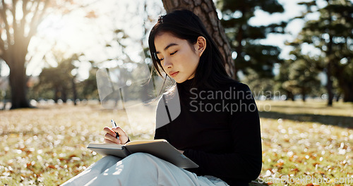 Image of Japanese woman, writing and book in park, thinking and relax by tree, grass or sunshine for peace. Girl, person or student with story in nature, college or notes with vision, knowledge or campus lawn