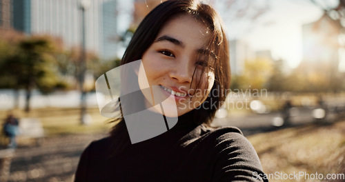 Image of Japanese woman, happy and portrait in park, nature and path with sunshine, city and buildings with pride. Girl, person and smile by lawn, grass and trees in urban metro, outdoor and travel in Tokyo