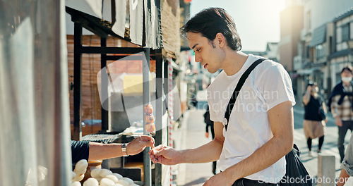 Image of Man, food and street vendor with kebab on travel, walk or tourism for taste test, culture and giving product. Person, customer and shop for snack on metro sidewalk, vacation and urban road in Japan