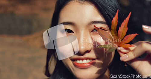 Image of Woman, Asian and face with leaf in autumn, nature and color with happiness outdoor. Environment, plant and smile in portrait, park or garden in Japan with foliage, mockup space and positivity