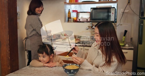 Image of Family, Japanese and mother feeding kid in kitchen of home for growth, health or nutrition. Food, daughter eating in Tokyo apartment with parent and grandparent for diet or child development