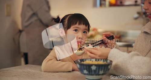 Image of Family, japanese and woman feeding daughter in kitchen of home for growth, health or nutrition. Food, girl eating in Tokyo apartment with mother and grandparent for diet or child development