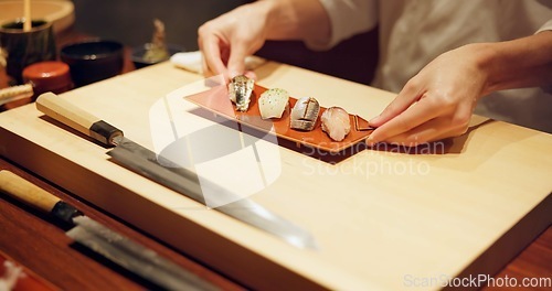 Image of Hands, food and chef serving sushi in restaurant for traditional Japanese cuisine or dish closeup. Kitchen, cooking or seafood preparation and person working on table with gourmet meal ingredients