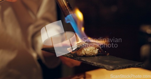 Image of Hand, sushi and fire with chef in kitchen of restaurant for luxury or traditional cuisine closeup. Food, blow torch and cooking with person flame grilling fish or salmon for Japanese seafood meal