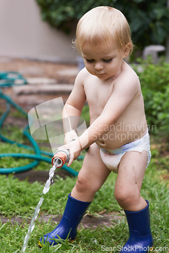 Image of Baby, playing with hose and water, backyard and development with growth, curiosity and home. Toddler, child and infant in garden, alone and childhood for wellness, milestone and coordination