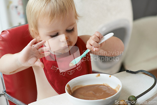 Image of High chair, eating and baby with spoon in a house for nutrition, diet and fun while playing. Food, messy eater and boy kid at home with meal for child development, fiber or vitamins while learning