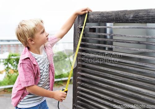 Image of Cute, measuring tape and portrait child doing maintenance on wood gate for fun or learning. Happy, equipment and young boy kid working on repairs with tool for home improvement outdoor at house.