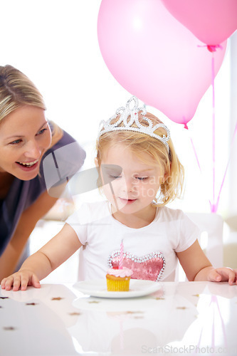 Image of Birthday, girl and mother with cupcake, candle and balloons for party, celebration and fun. Toddler with princess tiara, cake or dessert and woman with child at family home for milestone and event