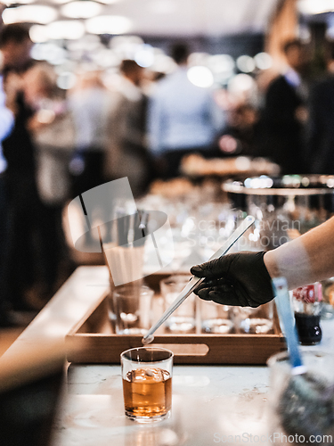 Image of Expert barman is making cocktail at business banquet event in hotel conference center. Blurred businesspeople at banquet event business meeting event in the background
