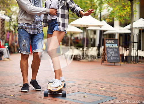 Image of Skateboard, legs and couple of friends teaching partner how to ride, exercise lesson or training in urban city. Fun activity, cardio fitness and feet of people helping, support and coaching to skate