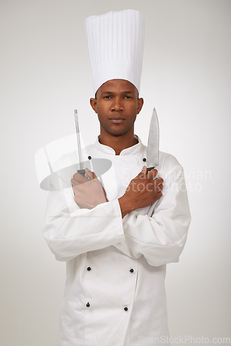 Image of Portrait, african chef and knives in studio in hospitality career and confident cook in food industry. Black man, face and serious in skill in kitchen utensils and uniform by hat by white background