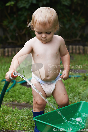 Image of Baby, playing with hose and gardening, water and development with bucket, curiosity and backyard. Toddler, child and infant in garden, alone and childhood for skills, milestone and coordination