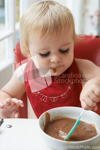 Image of High chair meal, spoon and baby eating in a house with diet, nutrition and child, wellness or development. Food, messy eater and boy kid curious about breakfast porridge, playing or learning at home