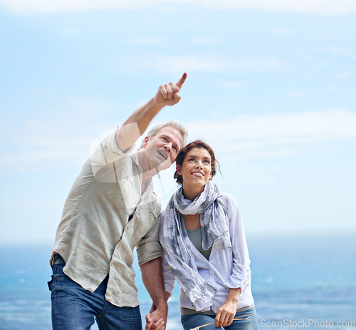 Image of Pointing, happy couple and travel together at the beach with love, adventure and summer. Vacation, man and woman holding hands and sightseeing at ocean, offshore or enjoy holiday with support or care