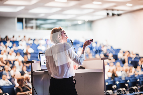 Image of Female speaker giving a talk on corporate business conference. Unrecognizable people in audience at conference hall. Business and Entrepreneurship event.