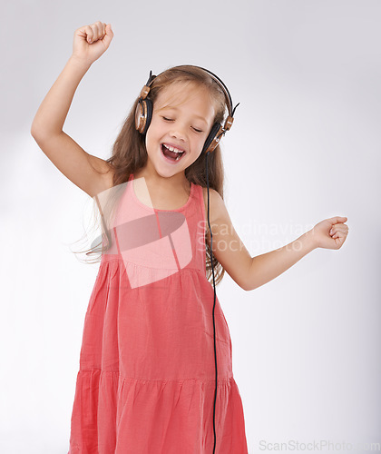 Image of Girl kid, dance and singing with headphones in studio for streaming audio, multimedia and celebration on white background. Excited young child with energy listening to music, hearing sound and radio