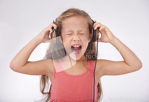 Image of Child, headphones and screaming in studio for music entertainment, rock or streaming. Female person, girl and shout for listening audio or radio noise or loud sing, white background or mockup space