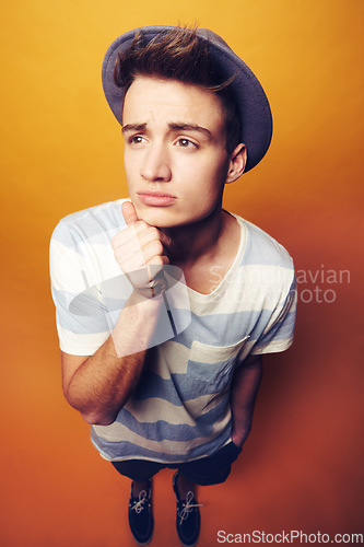 Image of Face, thinking and man with fashion hat and gesture in studio with confidence on orange background. Questions, emoji and male model with attitude, personality or trend, cool and fashionable outfit