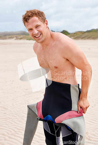 Image of Portrait, smile and surfer man in wetsuit at beach for sports, fitness or exercise on summer vacation. Travel, health and sand with happy young person getting for training, workout or surfing