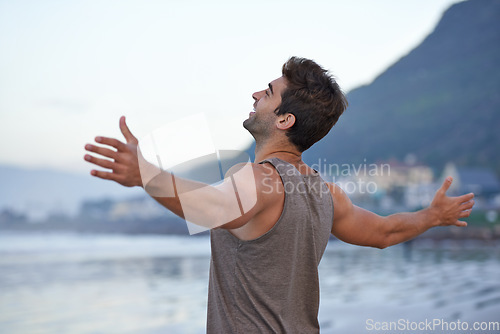 Image of Beach, happy and excited with man, holiday and journey with wellness and freedom. Person, outdoor and guy with arms raised, peace and happiness with vacation and adventure with journey and seaside