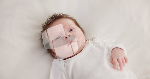 Image of Baby, calm face and above in the morning on nursery bed and blanket awake from nap and rest. Relax and newborn with happy smile on bedding from waking up from sleeping in a family home and bedroom