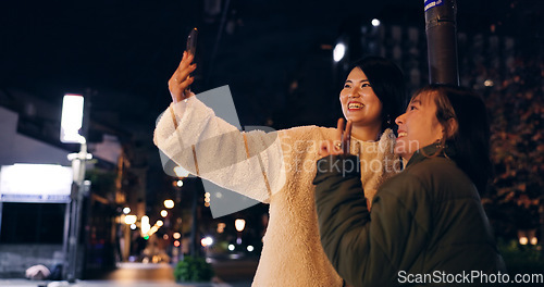 Image of Japanese, women and selfie outdoor at night with hand gesture, peace sign and happy in city street. Friends, people and phone with smile for travel, adventure and social media update in urban town