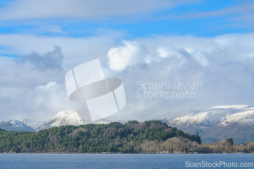 Image of Snow-capped mountains towering behind a dense forest by the calm