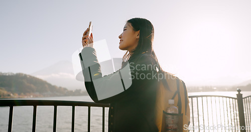 Image of Japanese woman, lake and phone for photography, memory and post on web blog for travel with backpack. Girl, person and outdoor with smartphone by water, river and photoshoot for social media in Tokyo