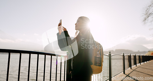 Image of Japanese woman, lake and phone for photography, memory and post on web blog for travel with backpack. Girl, person and outdoor with smartphone by water, river and photoshoot for social media in Tokyo