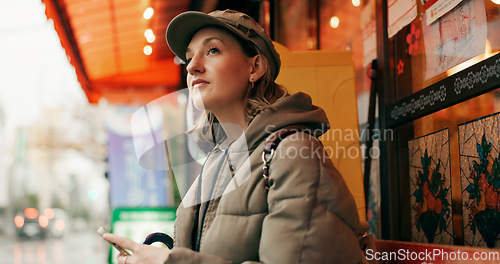 Image of Woman, street and waiting for taxi with phone in rain, thinking or winter for travel, transport and cab in city. Girl, person and smartphone in metro for bus, driver and chauffeur on road in Tokyo