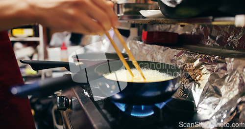 Image of Cooking, chopsticks and person with pan on gas stove at market for meal preparation, eating and nutrition. Culinary, flame and closeup of chef hands with utensils for egg cuisine, dinner and supper