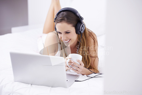 Image of Woman, bedroom and coffee on laptop for listening, watching and video streaming in headphones at home. Young person relax on bed with computer for morning news, social media or happy audio or podcast