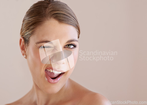 Image of Portrait, wink and skincare of woman in makeup at spa facial treatment to shine. Face, beauty and model in cosmetics for glow, health or wellness isolated on a brown studio background mockup space
