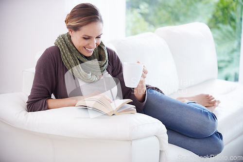 Image of Happy woman, book and reading with coffee on sofa for story, novel or knowledge in living room at home. Lady, fiction books and drinking cup of tea for literature, hobby or comfortable break on couch