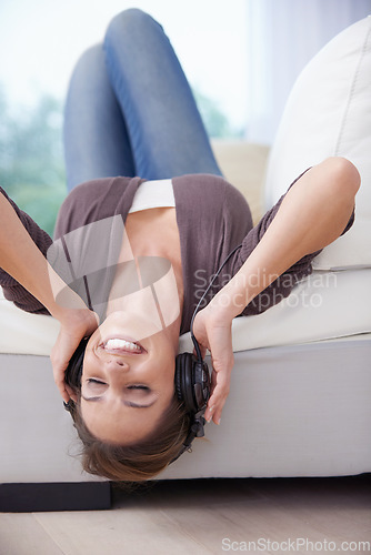 Image of Woman, upside down on sofa and headphones for music, audio streaming and happiness, stress relief and fun at home. Podcast, radio playlist and subscription online, relax in living room with tech