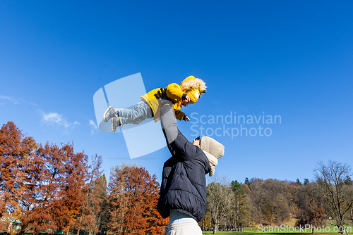 Image of More, more,...mum, that's fun. Happy young mother throws her cute little baby boy up in the air. Mother's Day, Mather and her son baby boy playing and hugging outdoors in nature in fall.