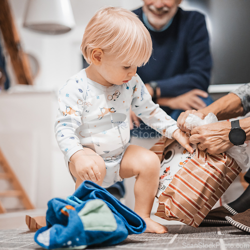 Image of Cute little blond Caucasian toddler unpacking Christmas or Birthday present. Adorable small infant baby boy opening gift