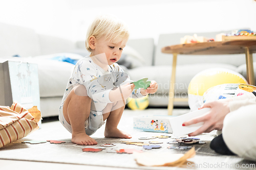 Image of Parents playing games with child. Little toddler doing puzzle. Infant baby boy learns to solve problems and develops cognitive skills. Child development concept