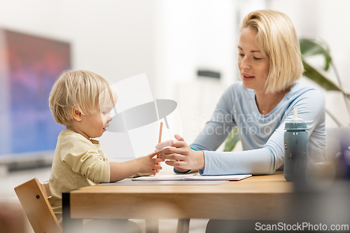 Image of Caring young Caucasian mother and small son drawing painting in notebook at home together. Loving mom or nanny having fun learning and playing with her little 1,5 year old infant baby boy child.