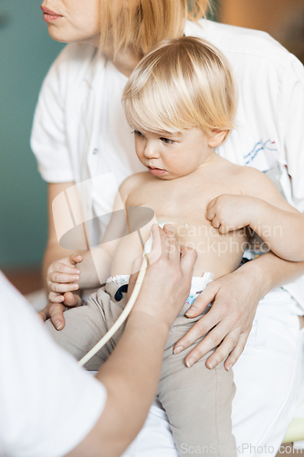 Image of Small child being checked for heart murmur by heart ultrasound exam by cardiologist as part of regular medical checkout at pediatrician.