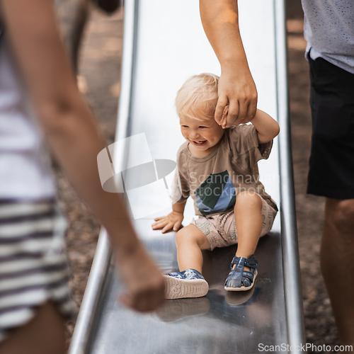 Image of Parent hand holding little infant baby boy child while sliding on urban playground on a sunny summer day. Family joy and happiness concept