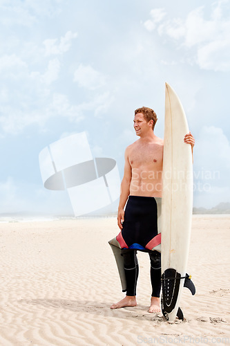 Image of Thinking, smile and shirtless man with surfboard on beach in wetsuit for sports, travel or fitness. Nature, vision and body of young surfer on sand by ocean or sea for exercise, training and workout