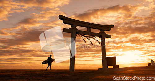 Image of Torii gate, sunset and man with surfboard, ocean and travel adventure in Japan with orange sky. Shinto architecture, Asian culture and calm beach in Japanese nature with person at spiritual monument.