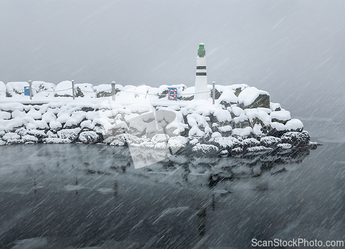 Image of A lighthouse stands resilient as snow covers the surrounding landscape amidst a winter storm.