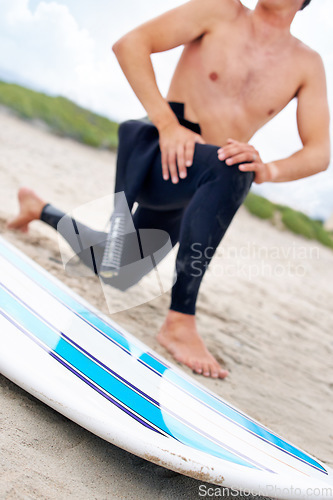 Image of Surfer, man stretching legs and surfboard on beach, fitness and extreme sport, ready for waves with travel and sand. Summer, wet suit and warm up, start surfing and nature with adventure outdoor