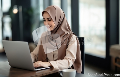 Image of In a cozy cafe, a woman in a hijab embraces modernity as she diligently works on her laptop, seamlessly blending technology with tradition in a contemporary and culturally diverse workspace