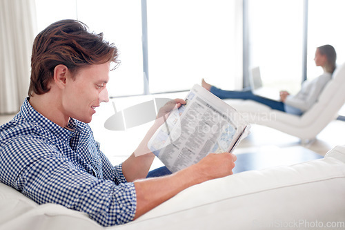 Image of Man, newspaper and reading on sofa with relax for story, article or information with smile in living room. Person, news and morning routine on couch with print media or knowledge for break in lounge